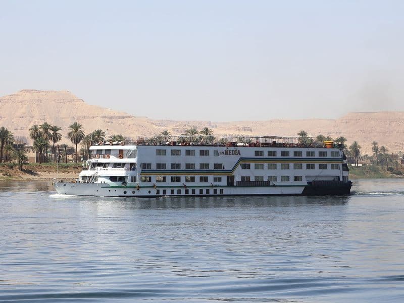 A Nile cruise ship sailing past palm trees and the Theban hills near Luxor